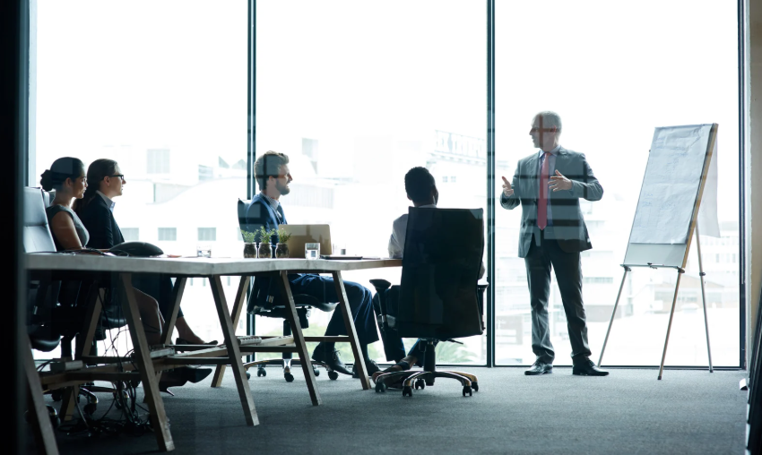 People sit in chairs at the office as someone delivers training at the front of the room.